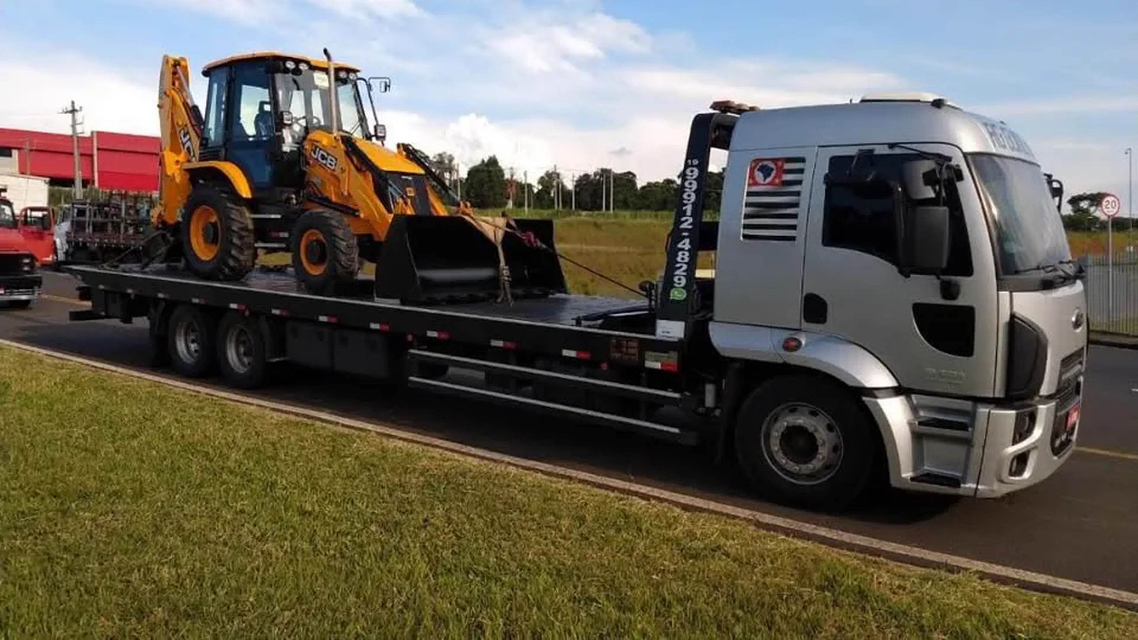 Caminhão prancha transportando retroescavadeira em operação