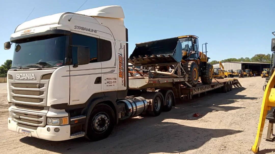 Caminhão prancha transportando equipamento de grande porte
