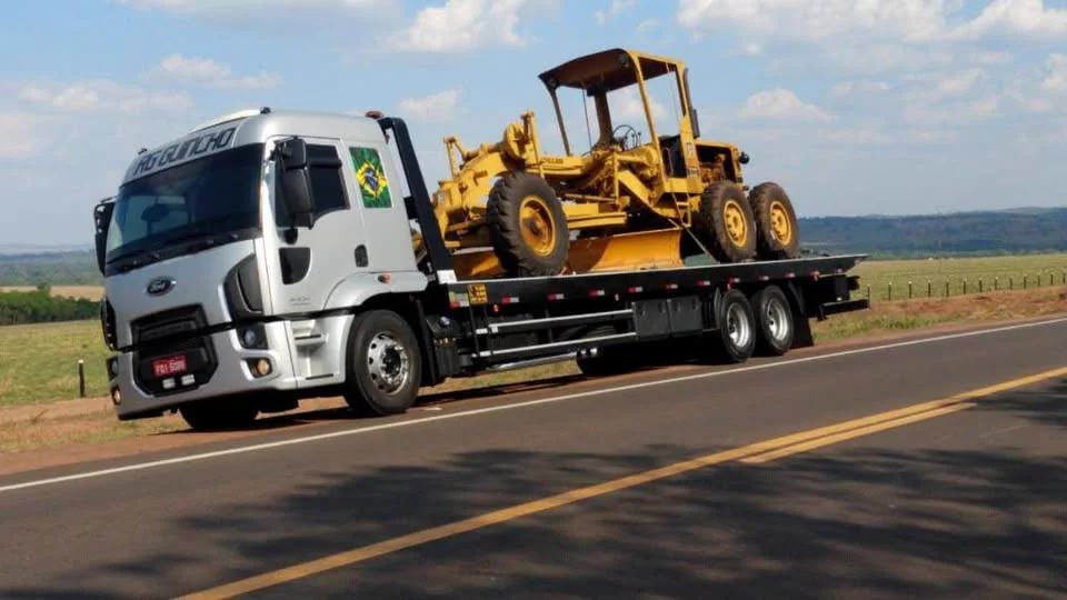 Caminhão prancha em rodovia transportando motoniveladora
